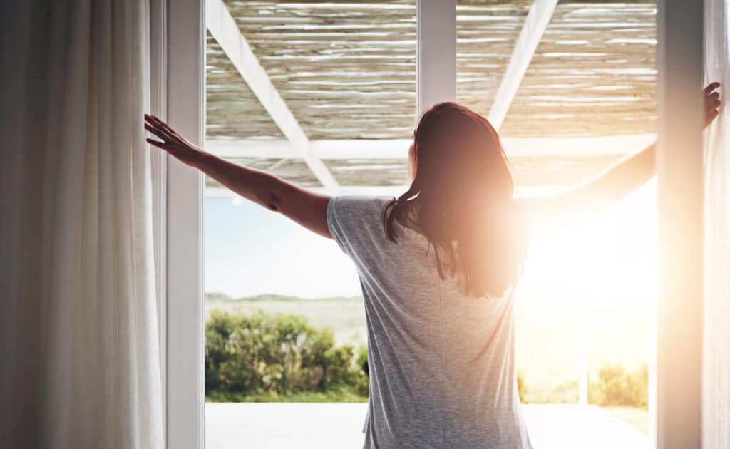 woman opening blinds to see sun rise