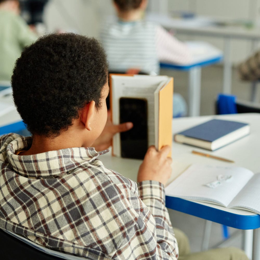 boy hiding phone behind textbook in class