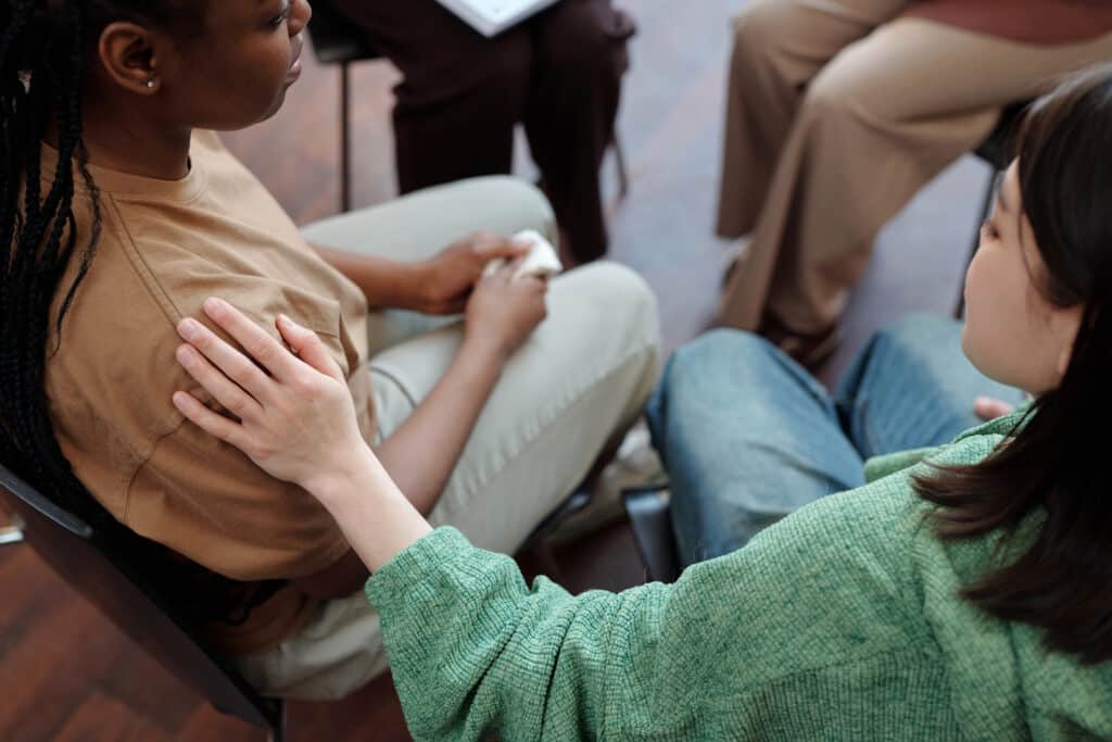 Young brunette women with hand on shoulder of upset African American women, comforting her during session
