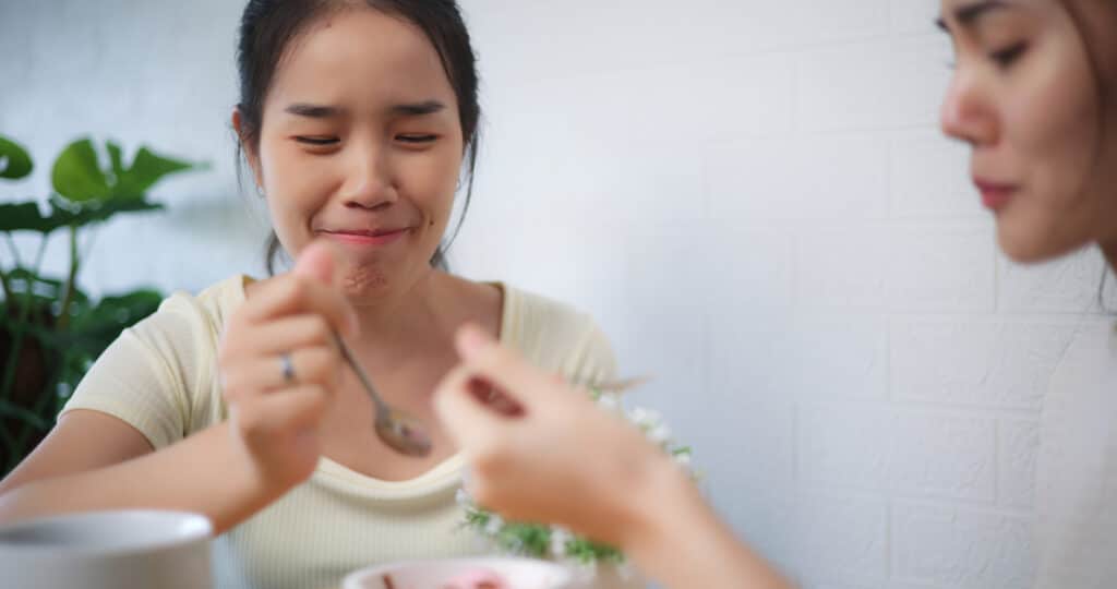 Cheerful Asian woman learning how to treat her ARFID sitting with her girlfriend having fun with talking while eating ice-cream together