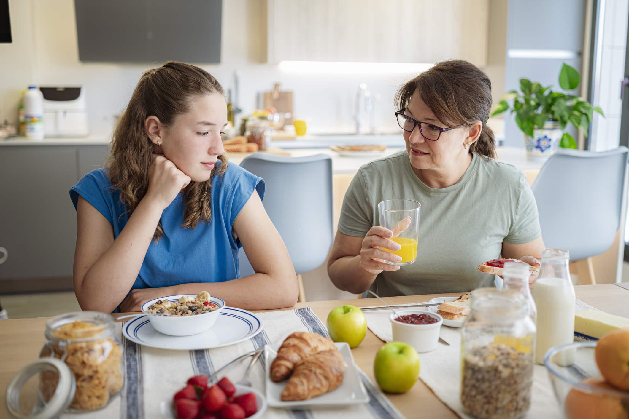 Mother and distraught teenage daughter having breakfast together