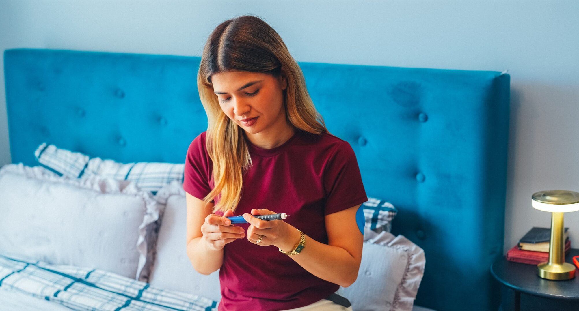 Young woman self administering BPC-157 peptide injection into abdominal area while sitting on bed at home. Recovery, regenerative medicine, biohacking and modern wellness concept.